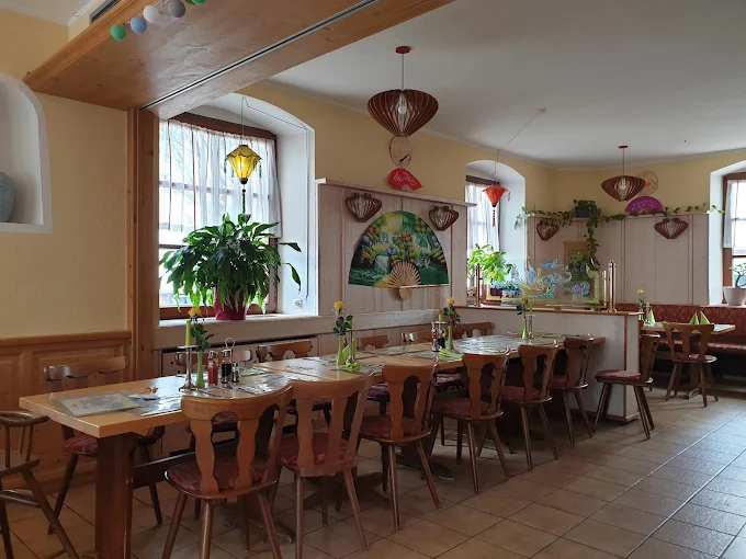 Die Gaststube des Annam: Holztische und Stühle, Lampions und vietnamesische Fächer an den Wänden, grüne Pflanzen am Fenster